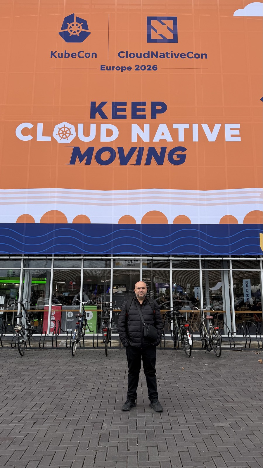 Diego Amorim em frente à entrada da KubeCon + CloudNativeCon Europe 2026 em Amsterdam